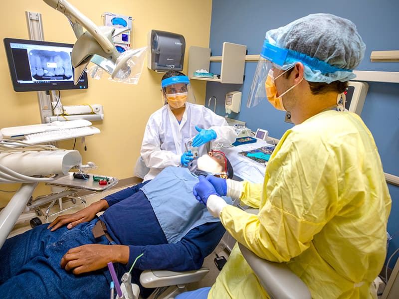 Dr. Deepti Janorkar, left, a School of Dentistry faculty member, instructs first-year dental resident Dr. Graham Garvey (‘21) as they treat Kelsey Kilpatrick of Grenada in the school’s Jackson Medical Mall dental clinic.